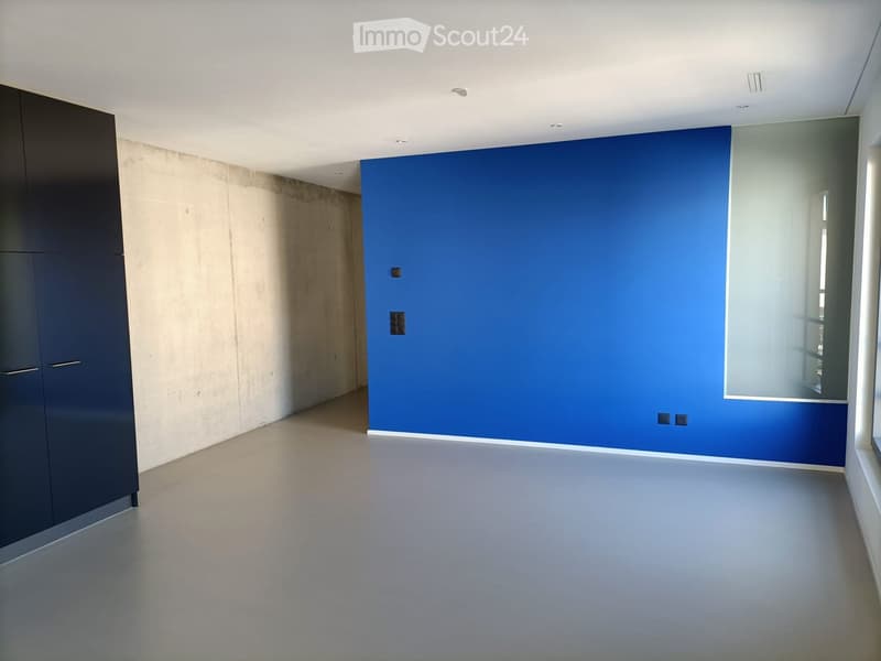 Empty room with smooth concrete walls, a large blue accent wall, and a dark cabinet on the left side.