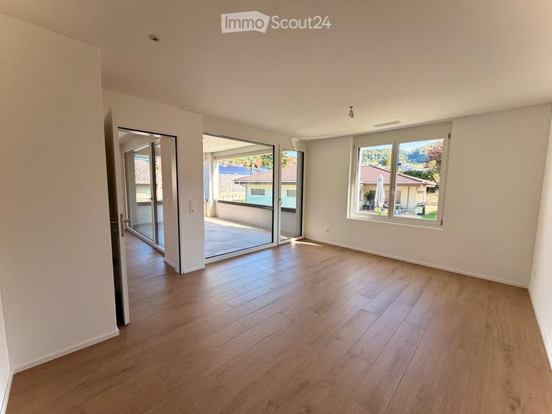 Empty room with wooden flooring, large windows, and sliding glass doors leading to a balcony.