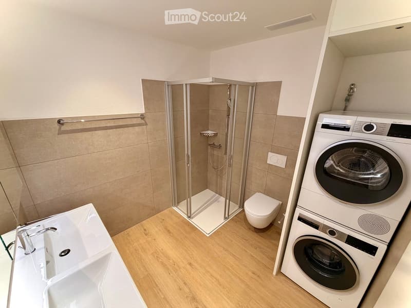 Modern bathroom with a bathtub, toilet, glass-enclosed shower, and stacked washer/dryer unit.