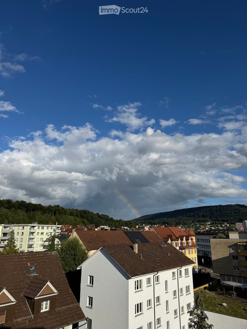 View of a residential area with multiple buildings, solar panels on rooftops, and a rainbow in the sky.