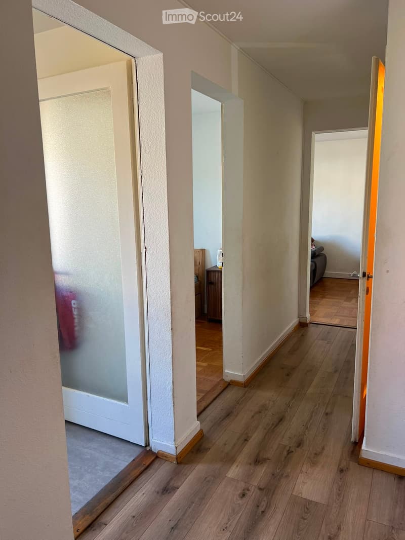 A narrow hallway with wooden flooring and white walls, featuring several open doors leading to adjacent rooms.
