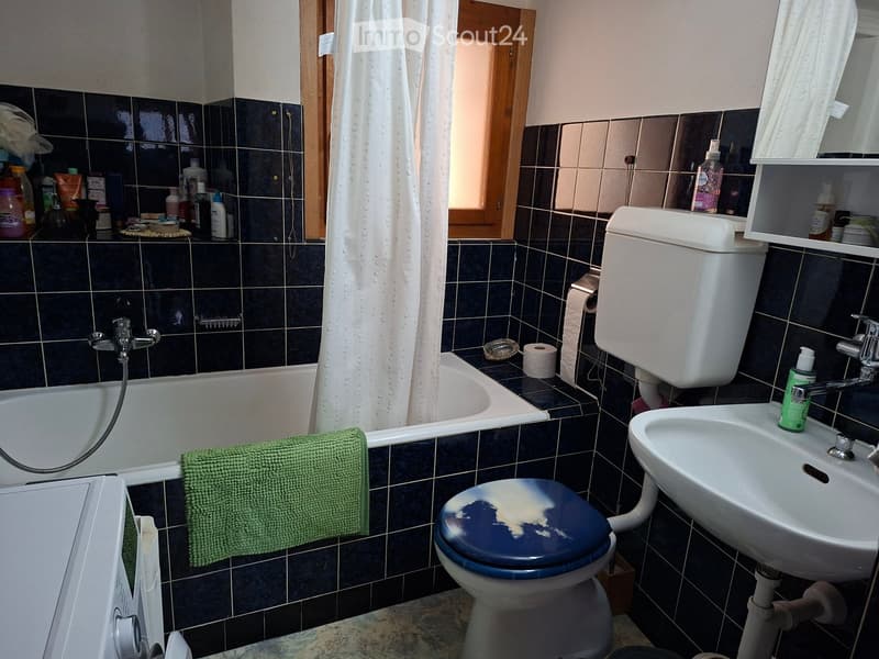 Bathroom with dark blue tiles, bathtub, toilet, sink, and various toiletries on shelves.