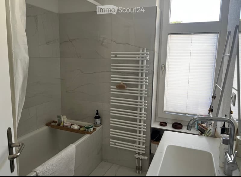 Modern bathroom with marble tiles, a bathtub, a sink, a radiator, and a towel on the edge of the tub.
