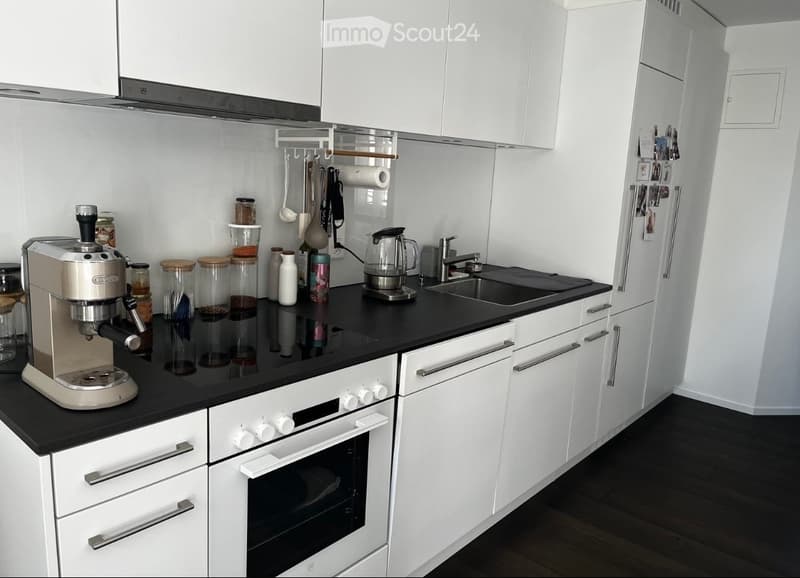 Modern kitchen with white cabinets, black countertops, stainless steel appliances, and various kitchen items on the counter.