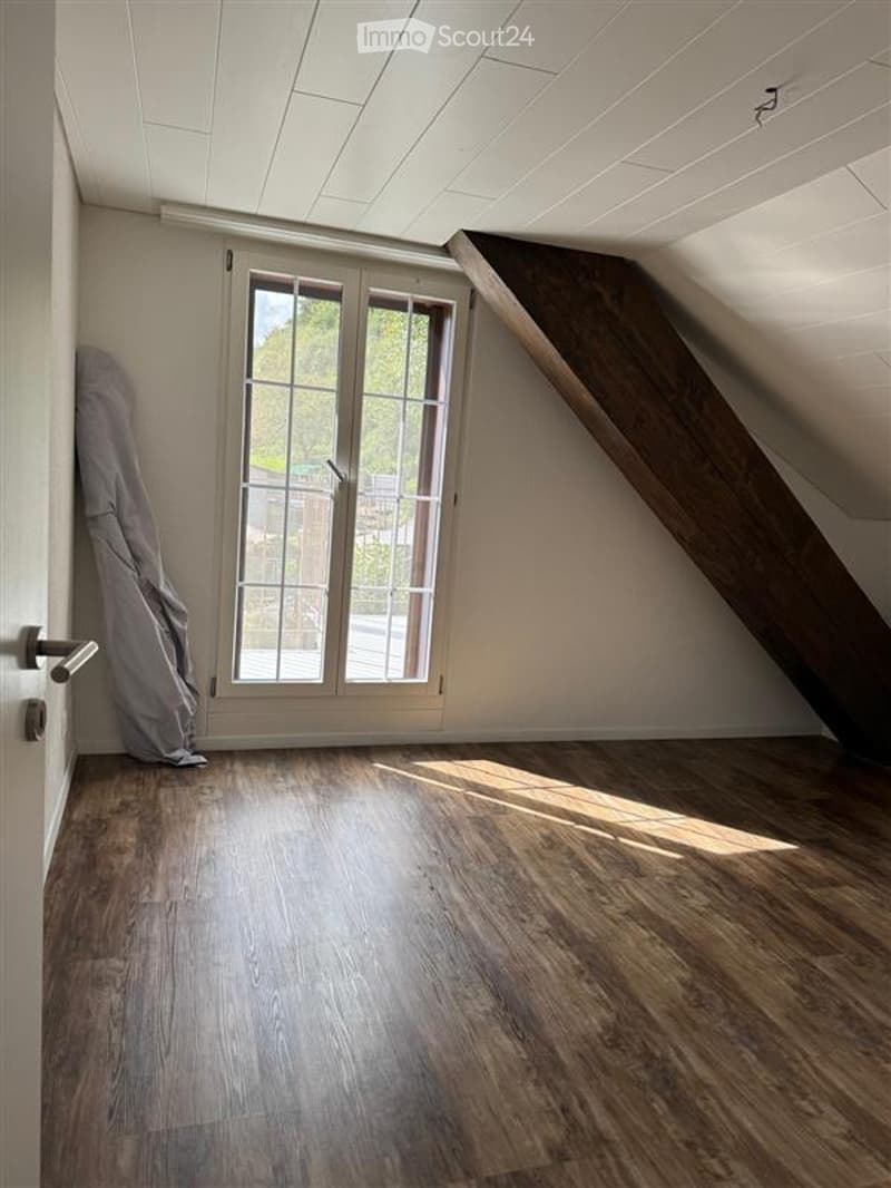 Empty attic room with windows, wooden floors, white walls, slanted ceiling.