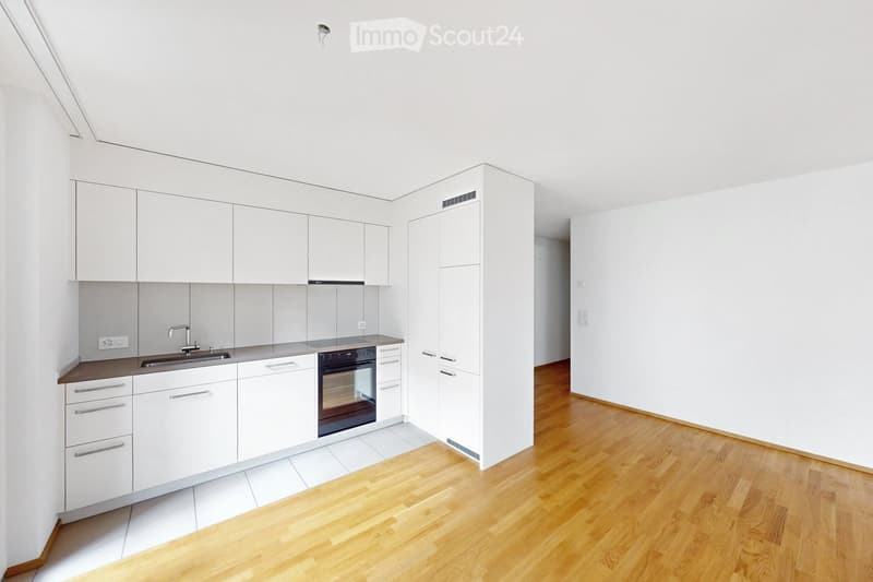 Modern kitchen with white cabinets, a stainless steel sink, and a built-in oven. The floor is light wooden, and the walls are white.