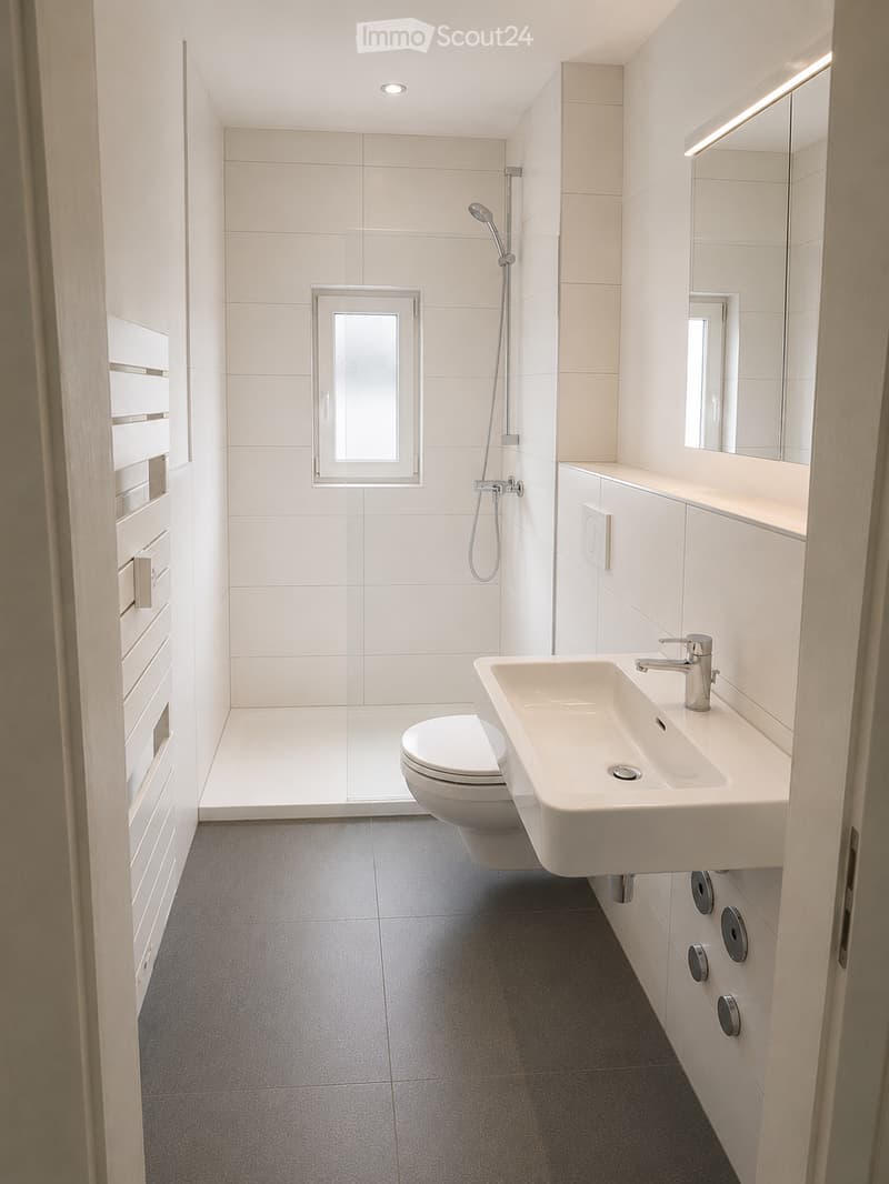 Modern bathroom with white tiles, a toilet, a sink with a modern faucet, a large mirror, and a shower area with a glass enclosure.