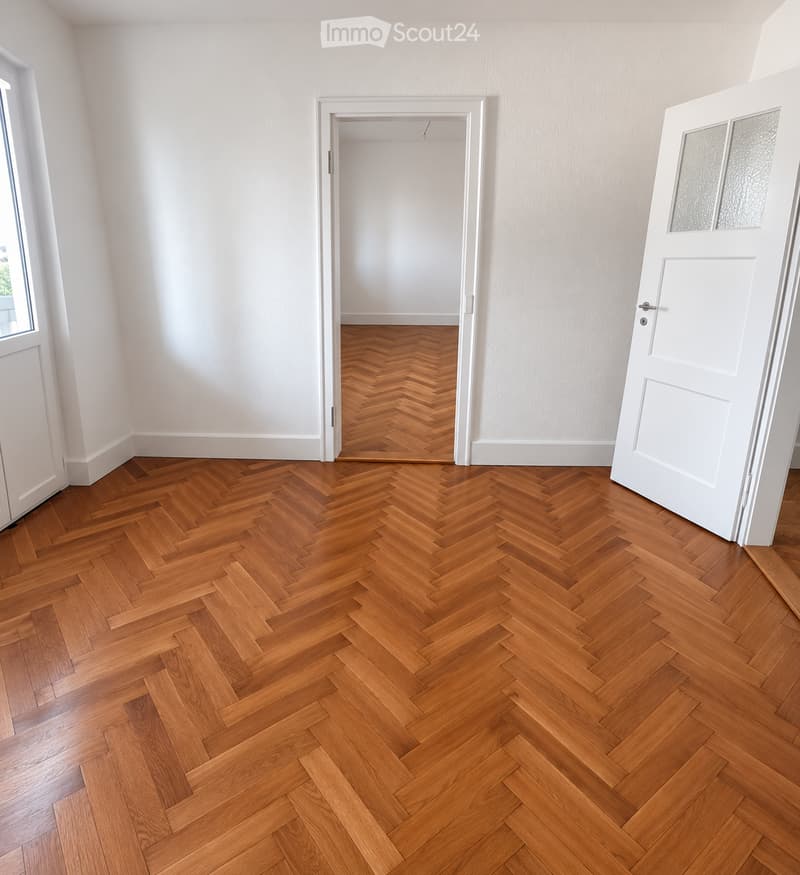 Empty room with herringbone-patterned wooden flooring, white walls, and white doors.