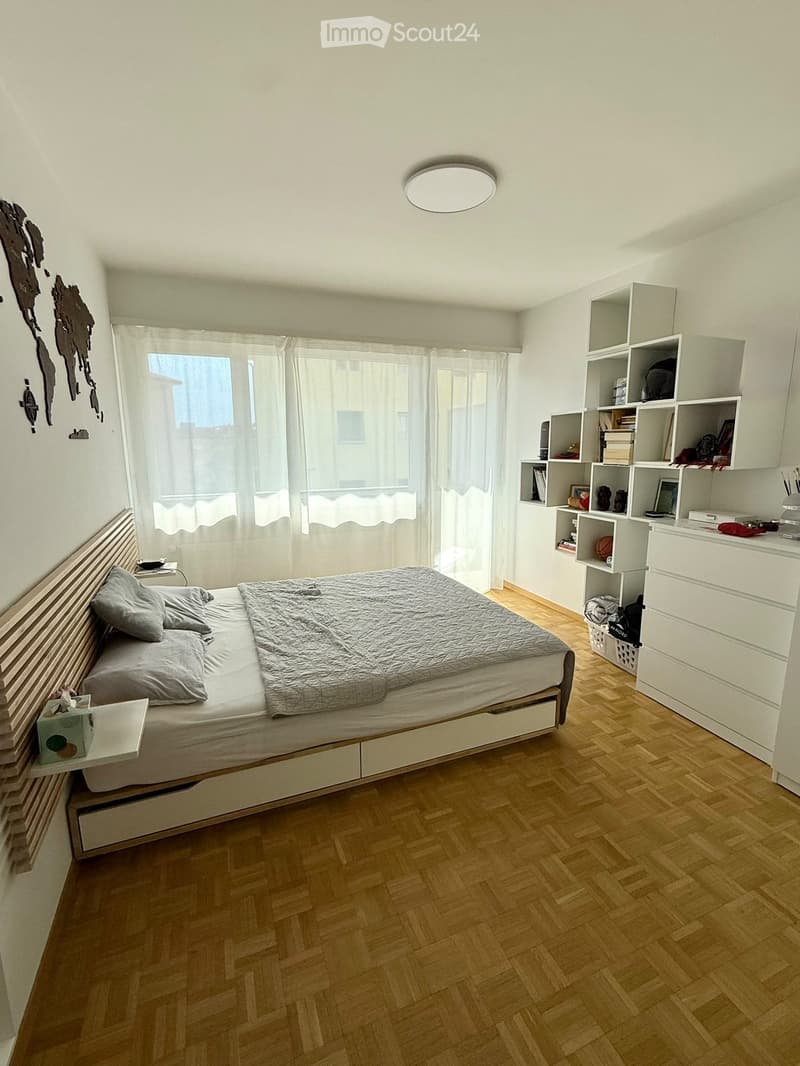 Modern bedroom with a large bed, nightstand, built-in shelves, and large windows with curtains.