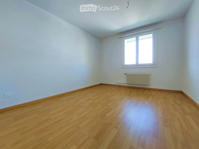Empty room with wooden flooring, white walls, and a window with white frame. A radiator is visible below the window.