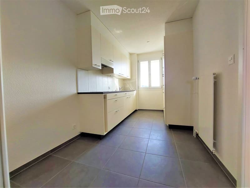 Modern kitchen with white cabinets, dark tiled floor, and a window at the end of the space.