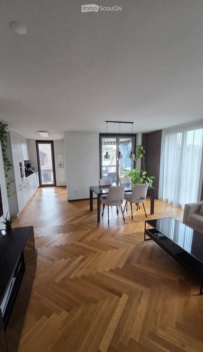 Open-plan living and dining area with wooden flooring, a sofa, coffee table, dining table with chairs, and a modern kitchen area with cabinets and appliances.