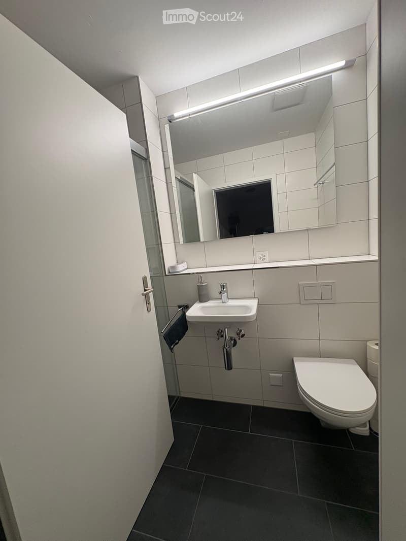 Modern bathroom with white tiles, a sink, a toilet, a large mirror, and a towel hanging on a rack.