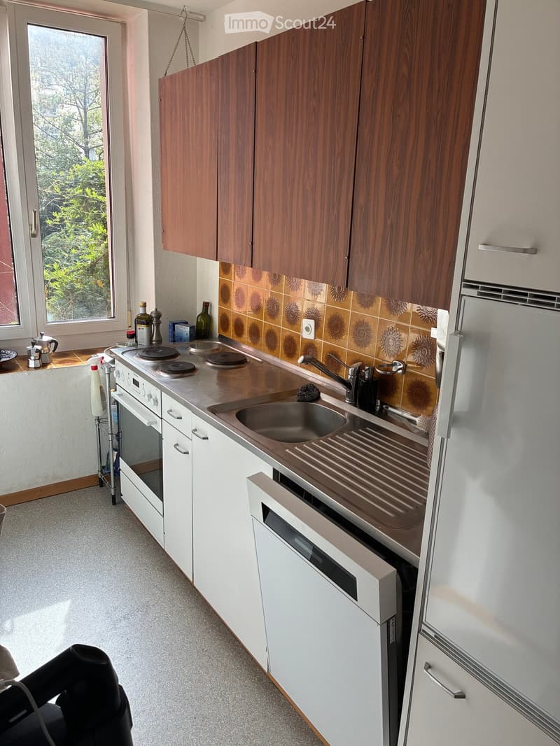 Modern kitchen with white and wooden cabinets, stainless steel sink, oven, and refrigerator. Countertop has a bottle and other small items.
