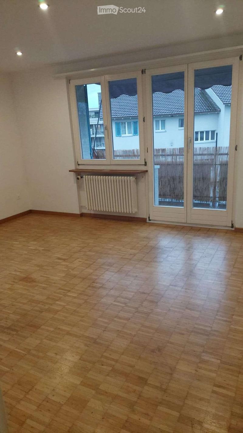 Empty room with wooden flooring, large windows, radiator, and sliding glass doors leading to an outdoor area.