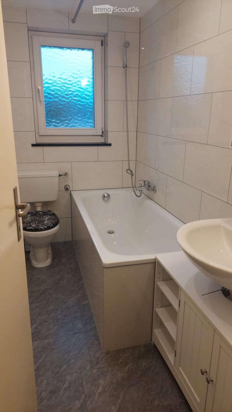 Bathroom with a bathtub, toilet, sink, and showerhead. The room features tiled walls and a window with frosted glass.