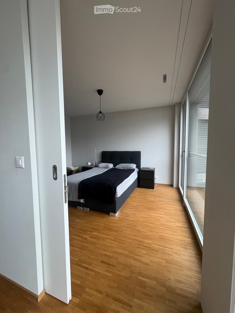 Modern bedroom with wooden flooring, a double bed with dark headboard, nightstands, and a pendant light fixture.