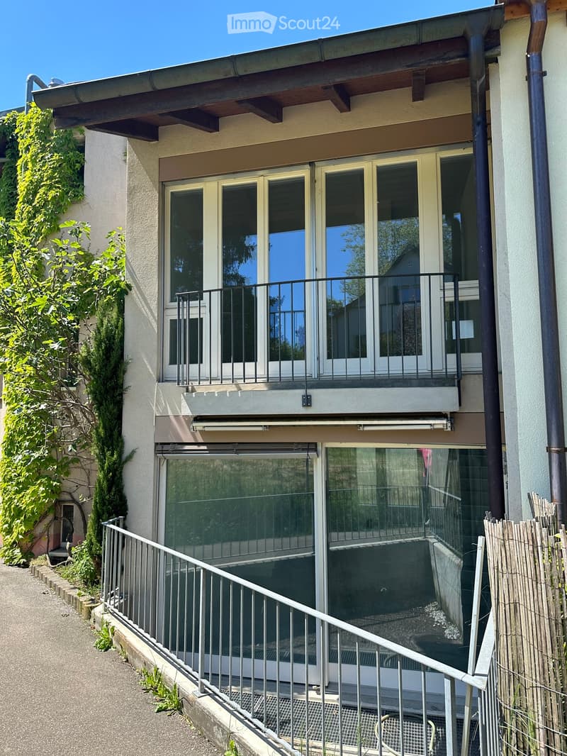 Two-story building with large windows, balconies, and a covered entrance area. The building has a modern design with a mix of glass and concrete elements.