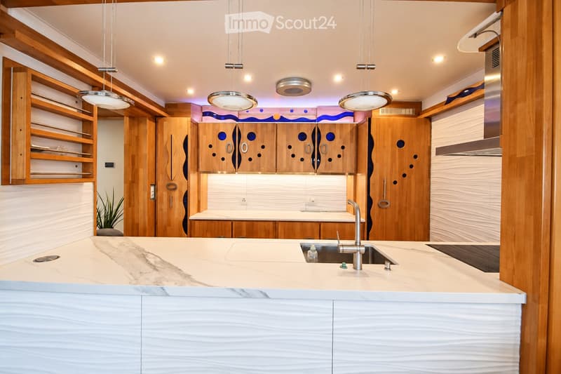 Modern kitchen with wooden cabinets, marble countertop, stainless steel sink, and pendant lights.