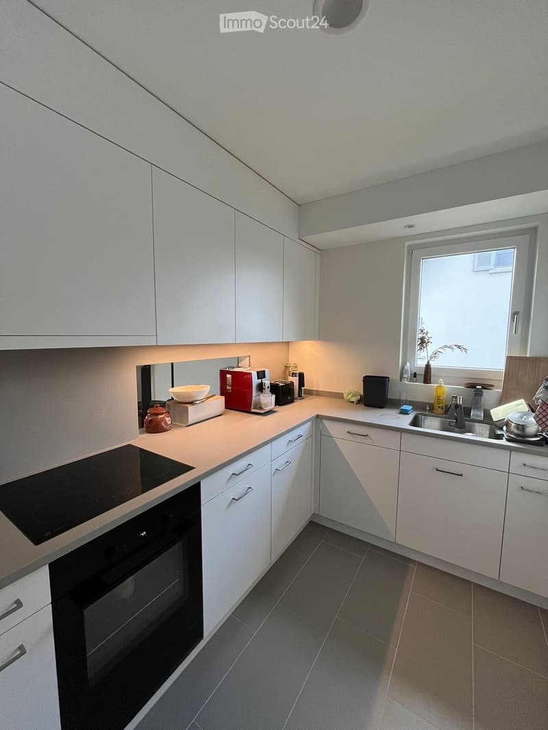 Modern kitchen with white cabinets, induction stove, oven, sink, and various appliances on the counter.
