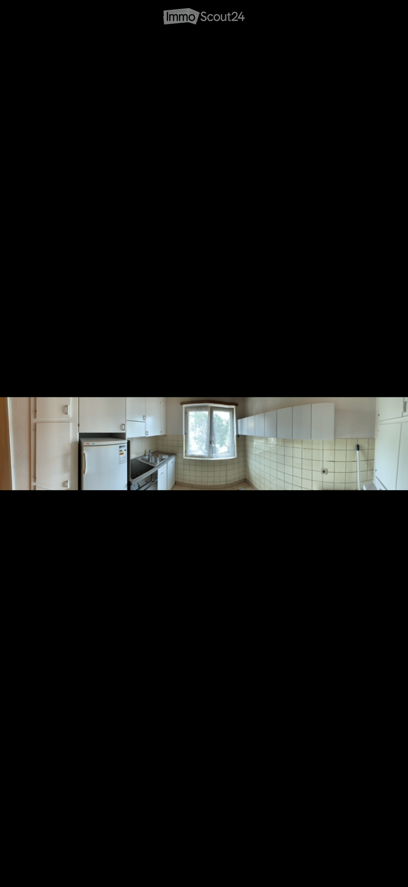 A small kitchen with white cabinets, a refrigerator, a sink, and a stove. The walls are tiled in a light green pattern, and there is a window above the sink.