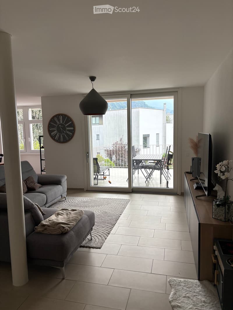 Modern living room with grey sofa, coffee table, television, and a large sliding glass door leading to a balcony.