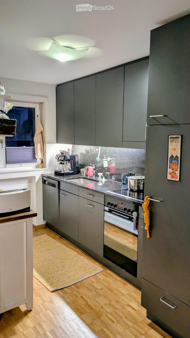 Modern kitchen with grey cabinets, stainless steel appliances, wooden flooring, and a window with blinds.