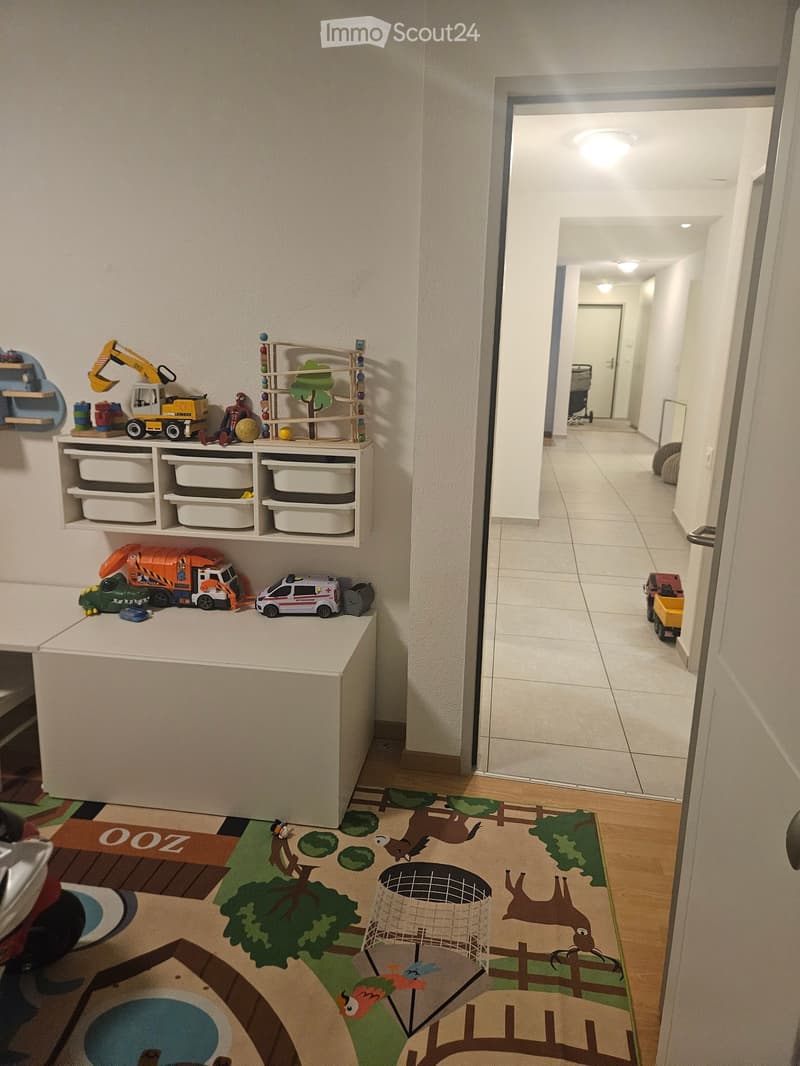 Hallway with tiled floor, white walls, and a colorful play area with toys and storage units on the left side.