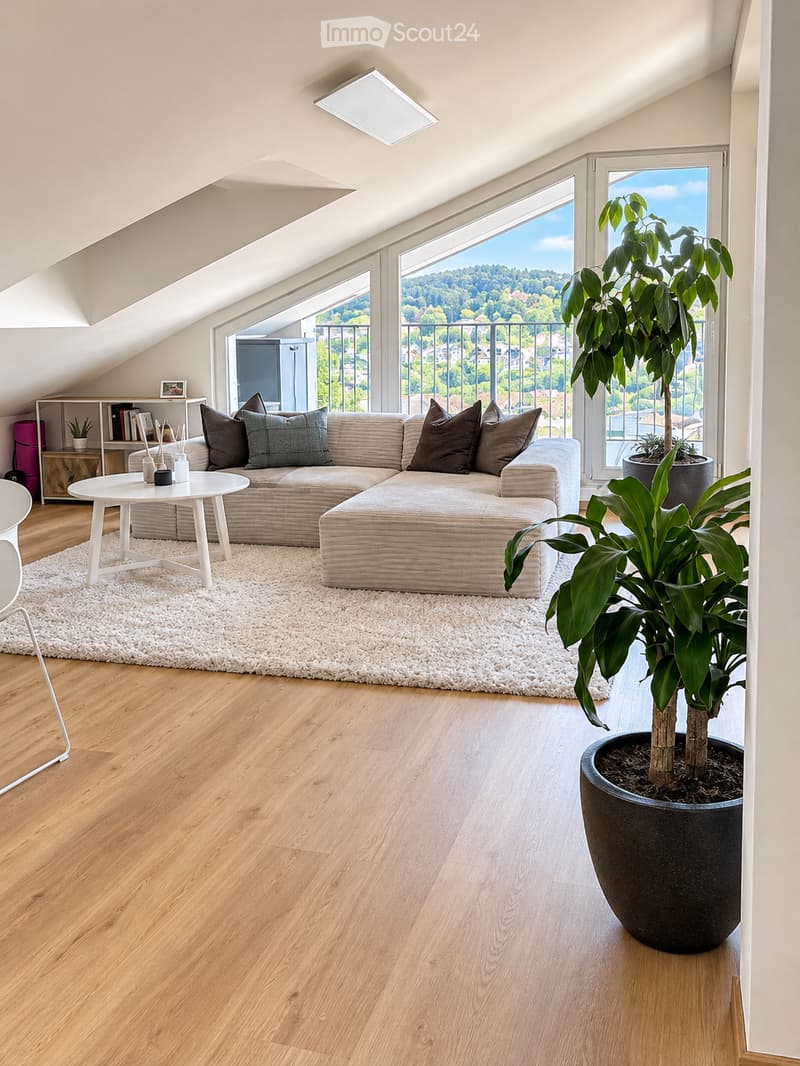 Modern living room with wooden flooring, large windows offering a scenic view, a sectional sofa, coffee table, and potted plants.