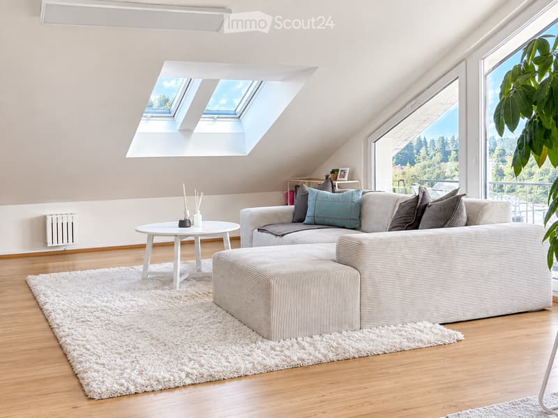Modern living room with a grey sectional sofa, white coffee table, ottoman, and large windows offering a scenic view.