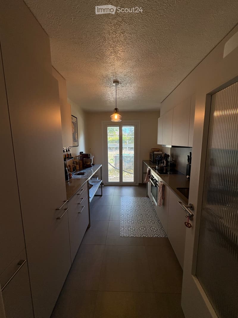 Modern kitchen with white cabinets, stainless steel appliances, a small rug, and a sliding glass door leading to an outdoor area.