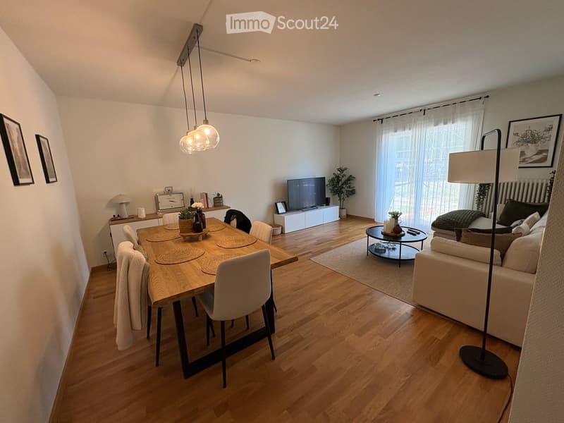 Open-plan living and dining area with wooden flooring, a sofa, dining table with chairs, a TV, and decorative items.