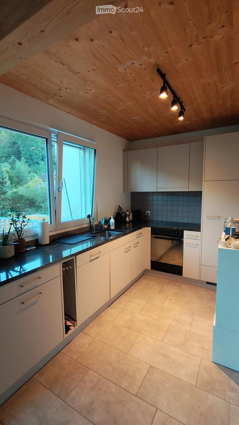 Modern kitchen with white cabinets, dark countertops, and a large window overlooking greenery. Features include a sink, oven, and various kitchen appliances.