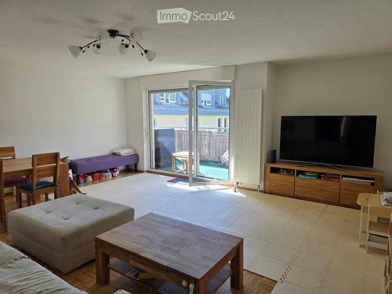 Bright living room with a sofa, coffee table, TV stand, dining area, and access to a balcony.