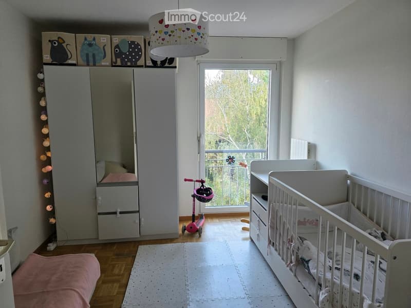 Brightly lit children's bedroom with a crib, wardrobe, scooter, and decorative lamp.