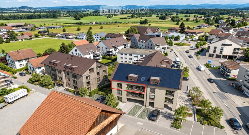 Aerial view of a residential area with multiple houses, surrounded by green fields and mountains in the background.