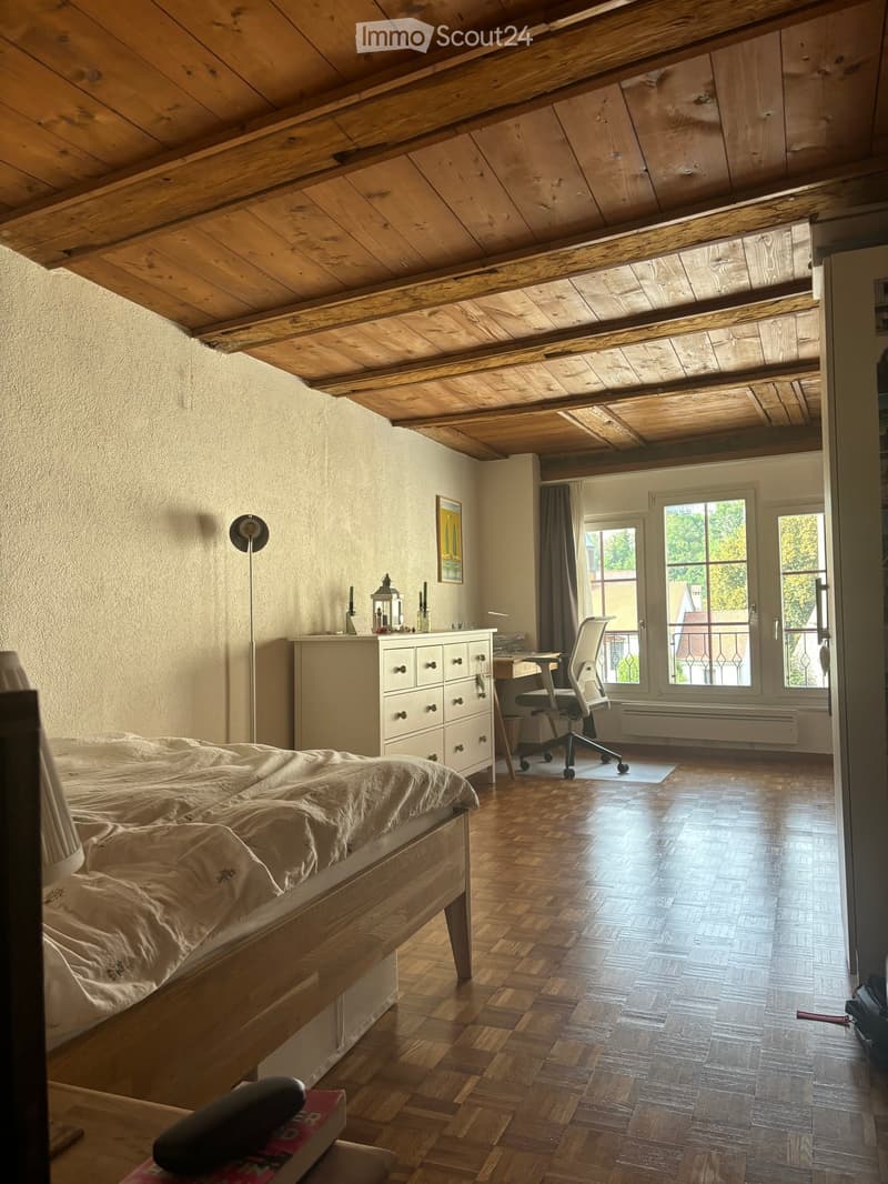 Cozy attic bedroom with wooden slanted ceilings, hardwood floors, a bed, a desk with a chair, a drawer unit, and a lamp.