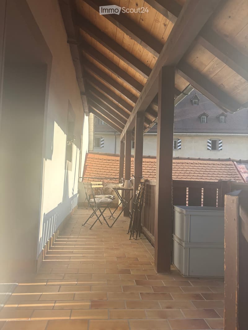 Balcony with wooden beams, tiled floor, and a small table and chairs set up.