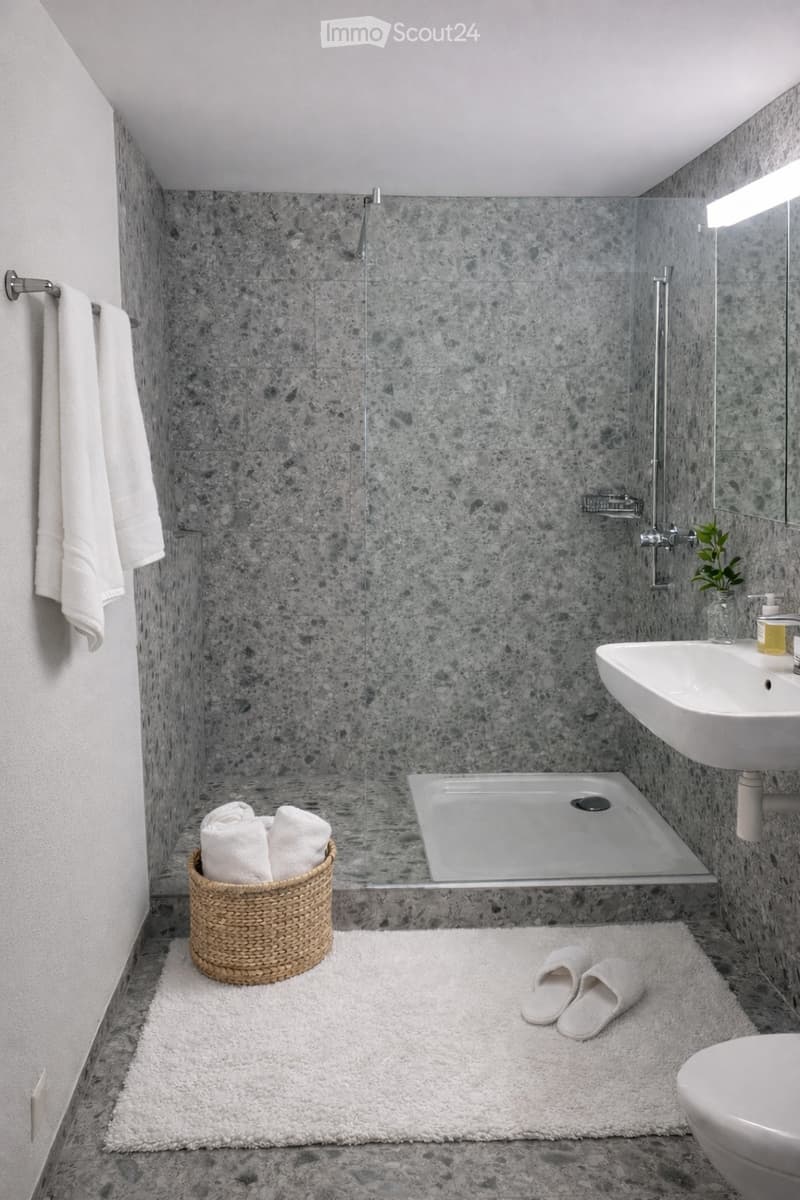A bathroom featuring a modern, stylish design with tiled floors and walls. A shower stall with a glass door and silver shower head is present. There is a white sink with a faucet and a mirror on the wall. Two white towels are on a towel rack and a wicker