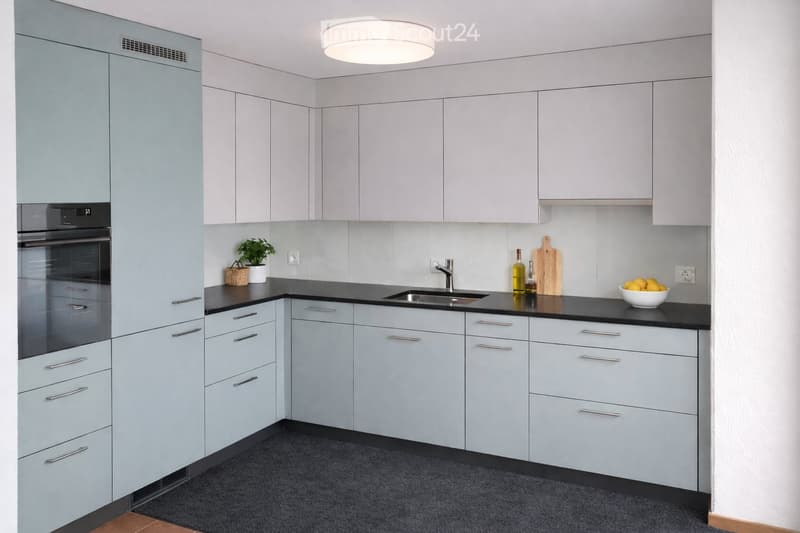 Modern kitchen with light grey cabinets, black countertops, stainless steel sink, and various small appliances and decorative items on the counter.