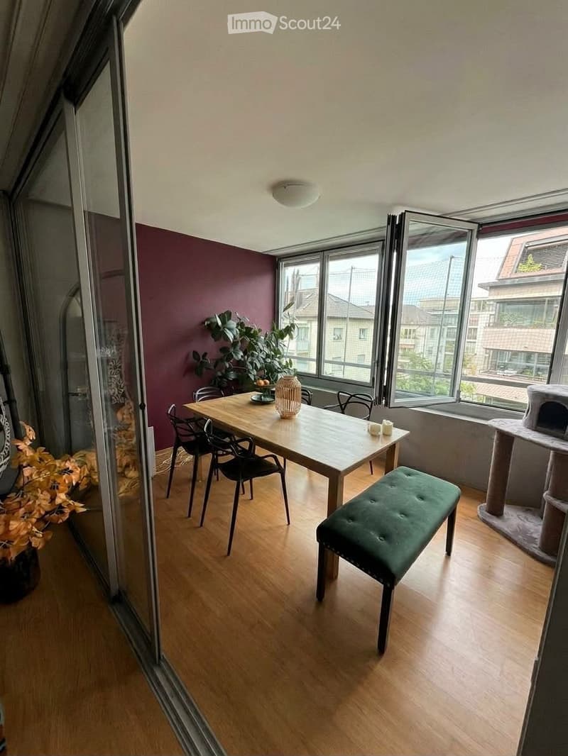 Dining area with wooden table, chairs, green bench, cat tree, and decorative vase with plant on table.