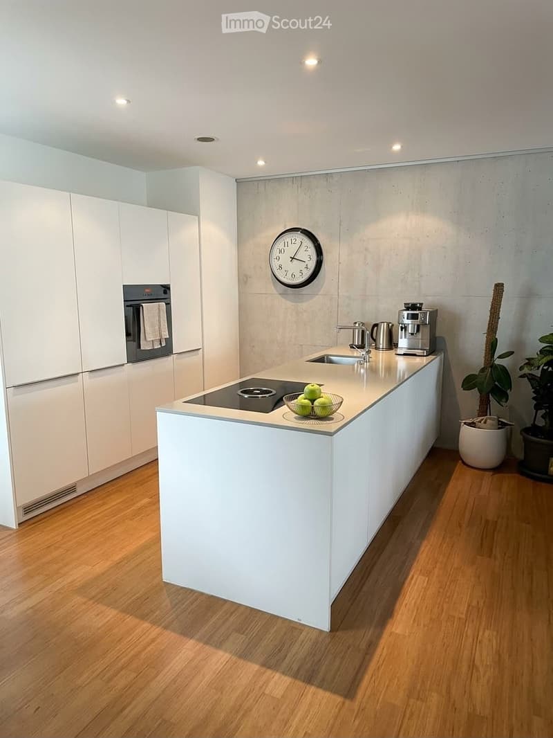 Modern kitchen with white cabinets, induction cooktop, sink, coffee maker, and a clock on the wall.