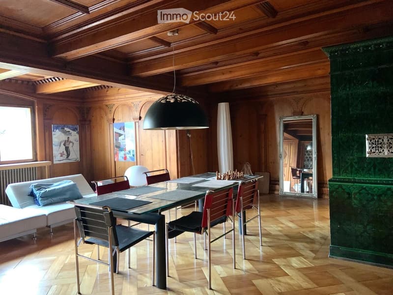 Elegant living and dining area with wooden beams, a large glass dining table, modern chairs, a white sectional sofa, and a large pendant lamp.