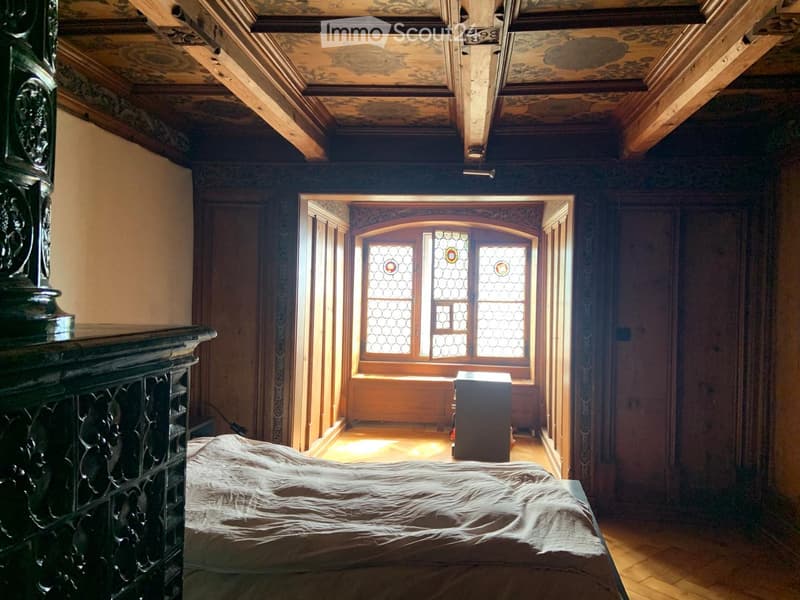 Elegant bedroom with wooden floors, ornate ceiling, stained-glass window, and a large bed with a white duvet.