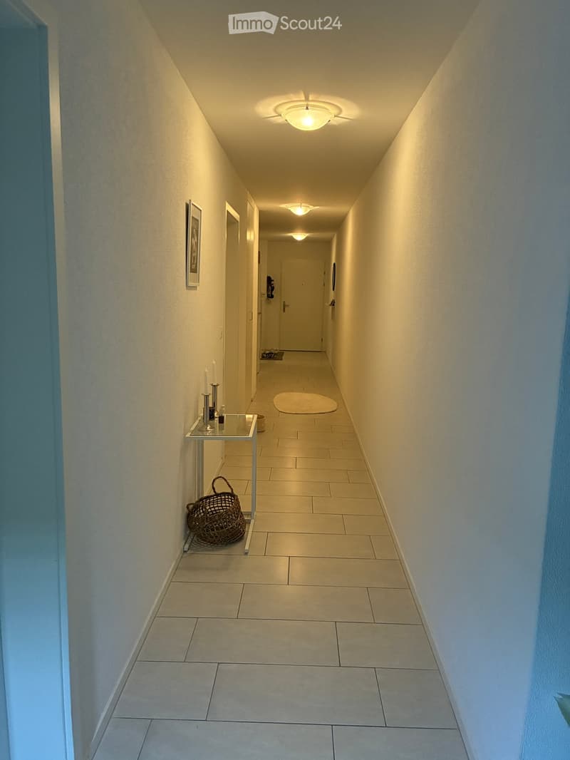 Clean hallway with tiled flooring, white walls, recessed lighting, and a small table with a basket and candles on one side.