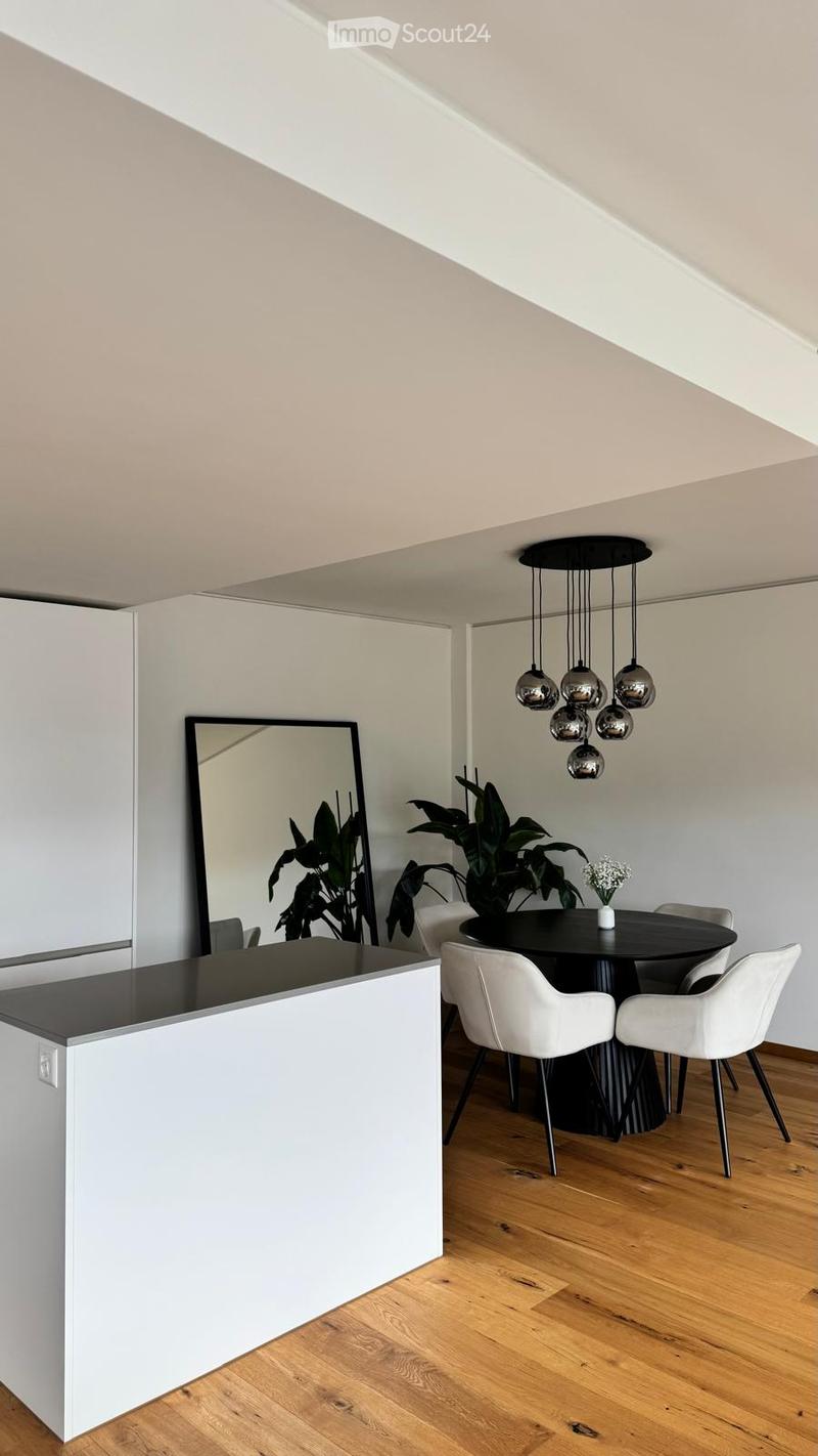 Modern dining area with a black round table, white chairs, a large mirror, and a hanging chandelier with spherical lights.