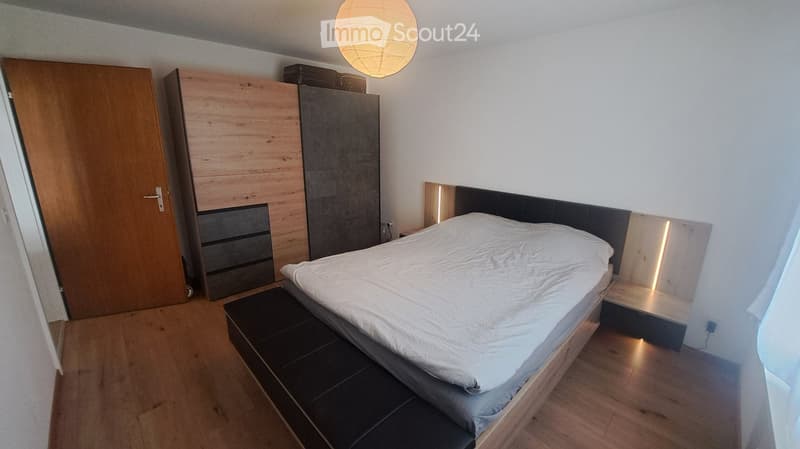 Modern bedroom with a wooden bed, white bedding, built-in wardrobe, and a hanging spherical lamp.