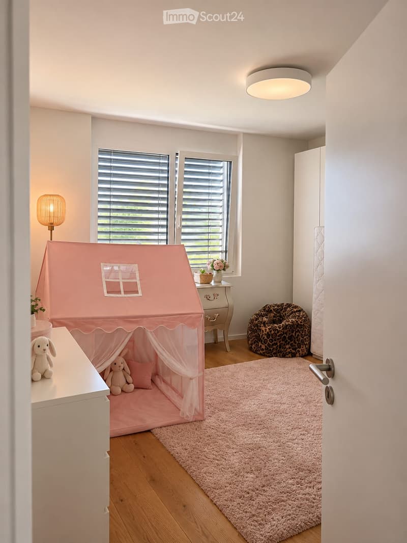 A cozy children's room with a pink play tent, stuffed animals, a beanie chair, a side table with a flower vase, and a table lamp.