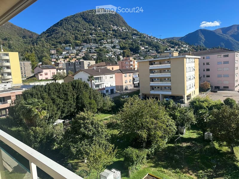 Balcony view overlooking a town with buildings, trees, and mountains in the background.