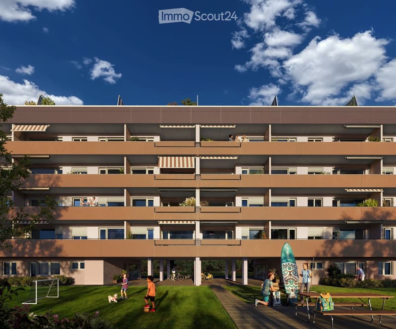 A modern multi-story residential building with balconies, surrounded by a green lawn and pathways. Children are playing on the lawn, and there are bicycles and a surfboard near the entrance.